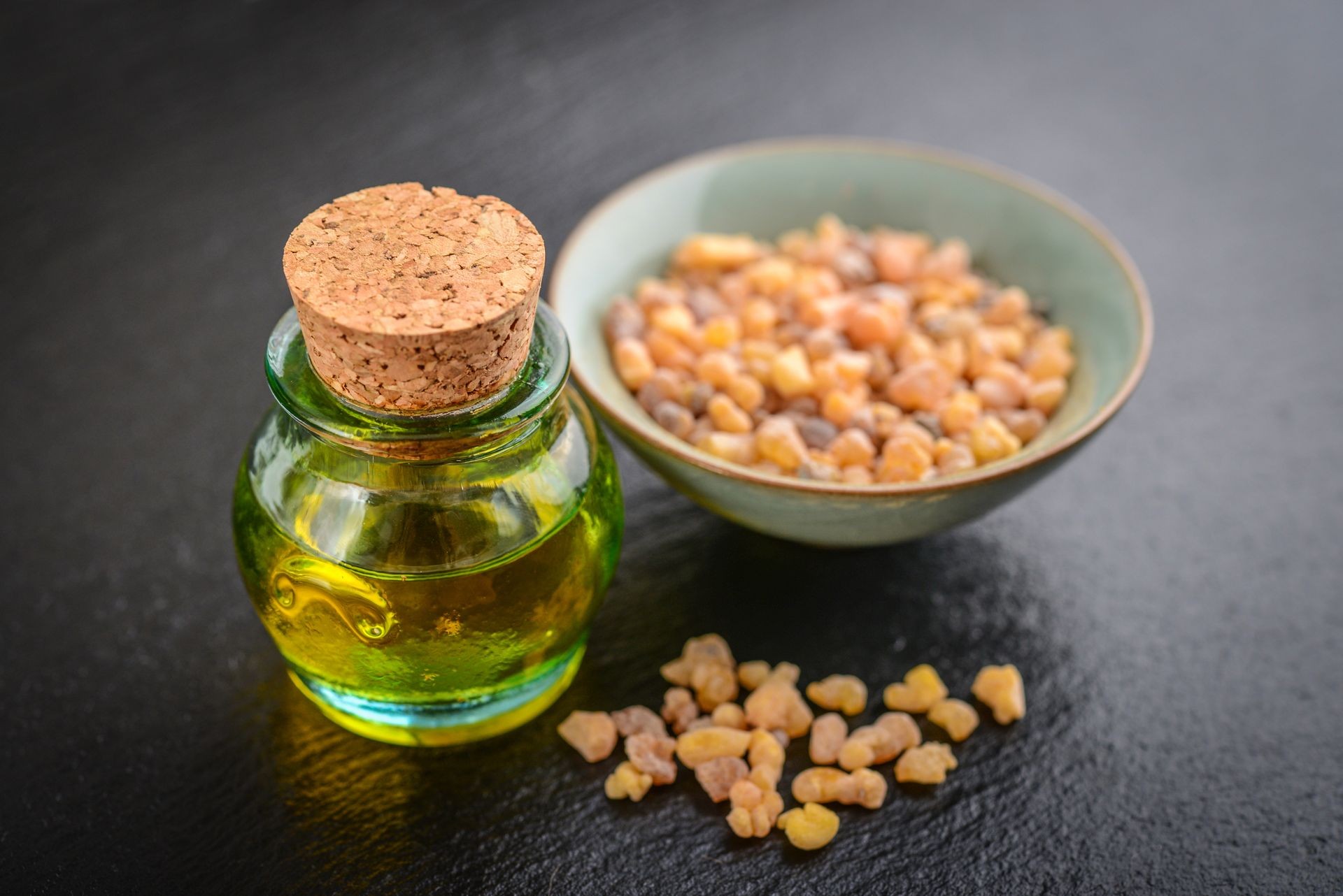 A bottle of frankincense essential oil with frankincense resin crystals on black slate background A bottle of frankincense essential oil with frankincense resin crystals on black slate background